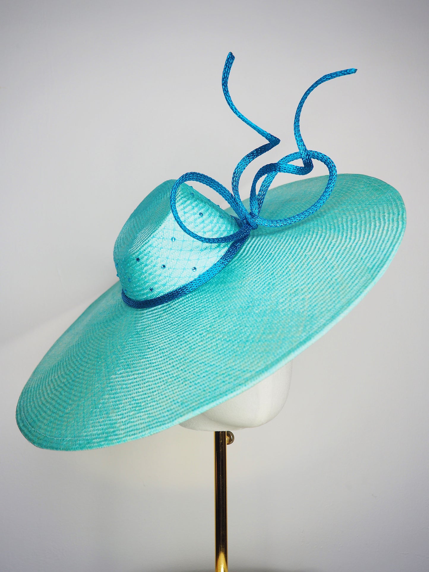 Sea Glass - A dramatic pale aqua asymmetrical brim featuring a sculptural turquoise bow, crystal detailing and delicate veiling.
