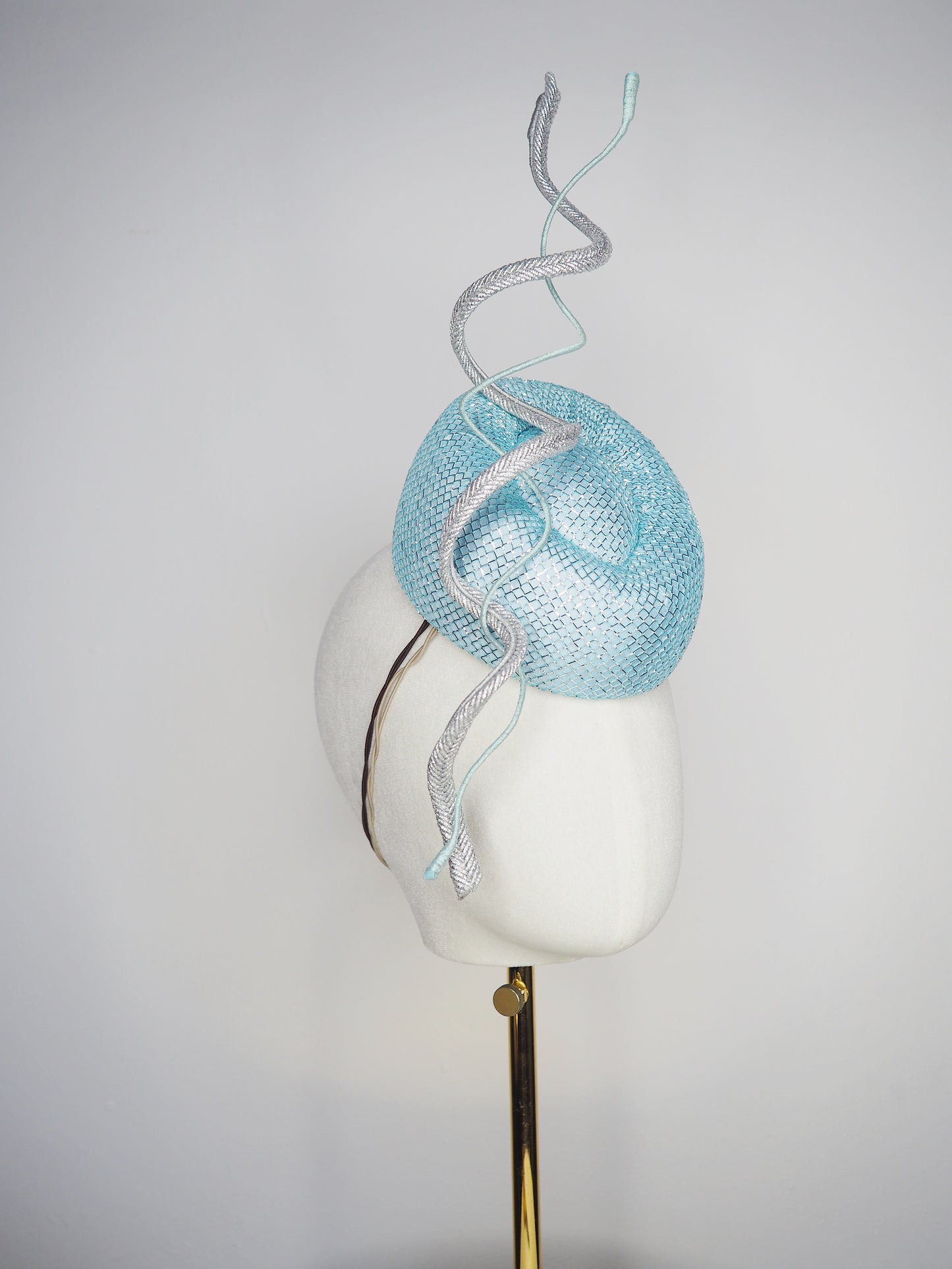 Blue Lagoon - A sophisticated pale aqua pillbox layered with shimmering lurex mesh and sculptural metallic swirls.