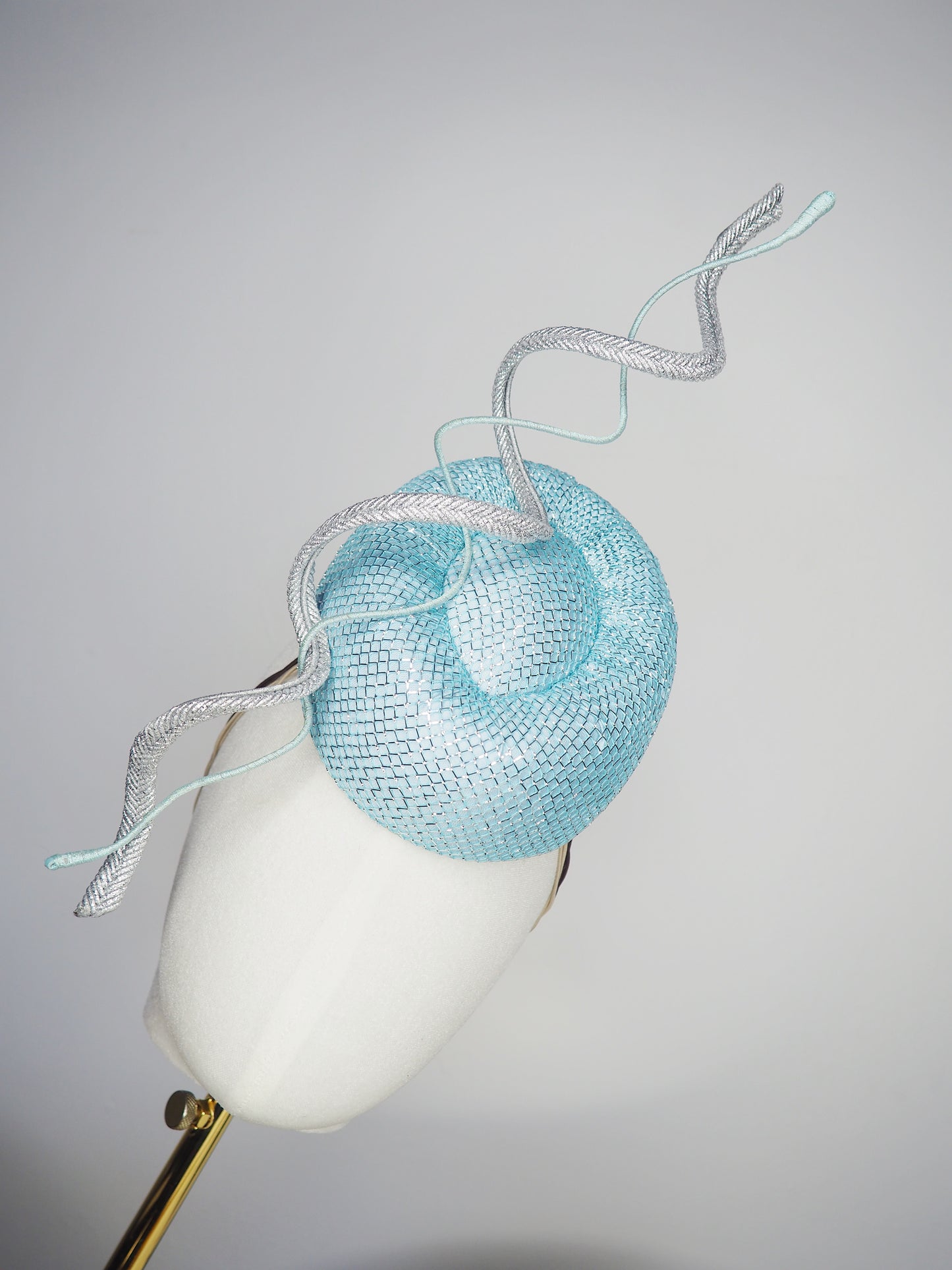 Blue Lagoon - A sophisticated pale aqua pillbox layered with shimmering lurex mesh and sculptural metallic swirls.
