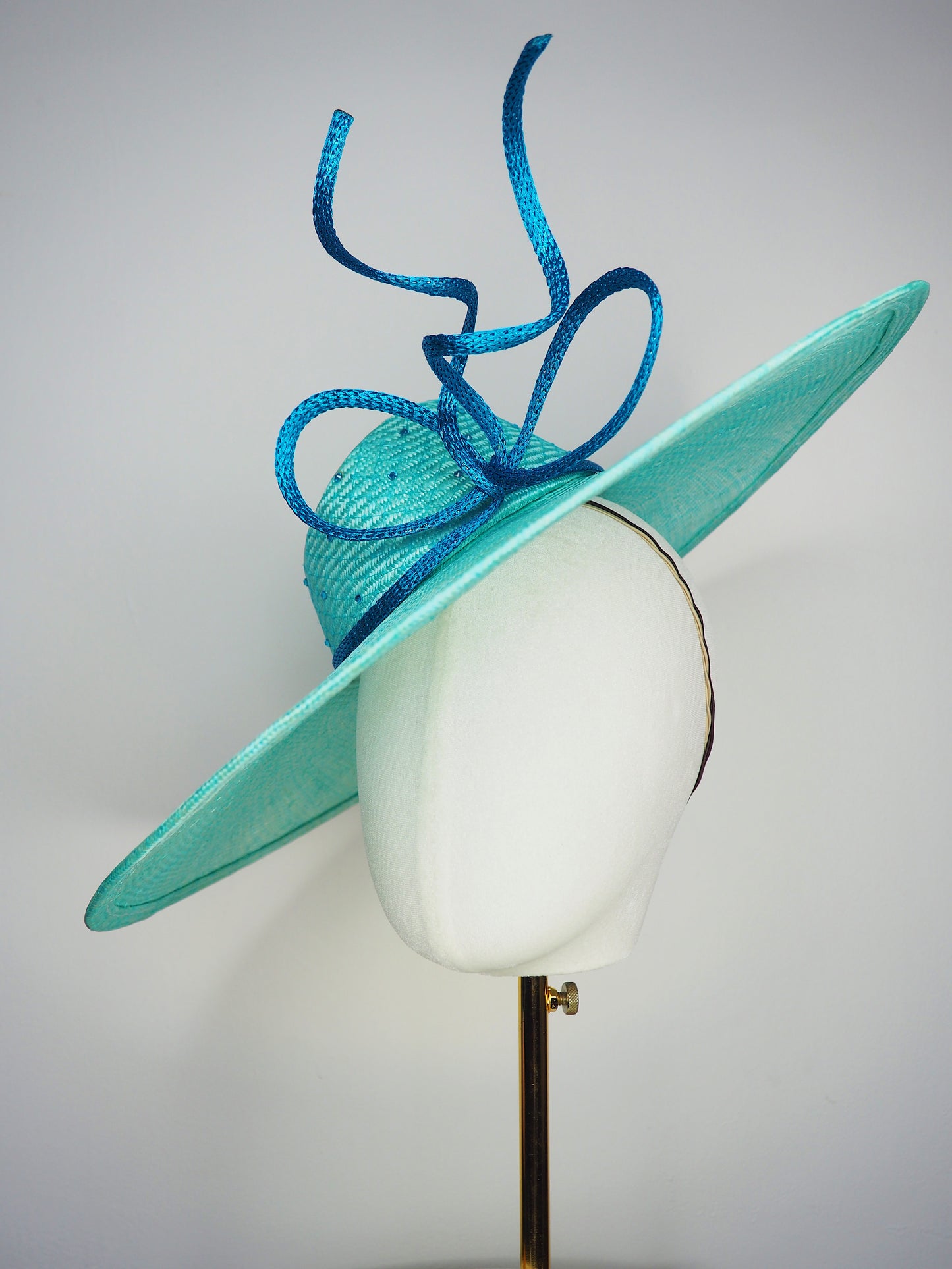 Sea Glass - A dramatic pale aqua asymmetrical brim featuring a sculptural turquoise bow, crystal detailing and delicate veiling.