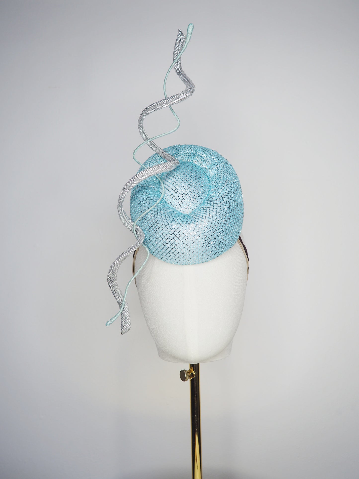 Blue Lagoon - A sophisticated pale aqua pillbox layered with shimmering lurex mesh and sculptural metallic swirls.