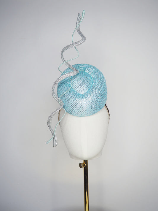Blue Lagoon - A sophisticated pale aqua pillbox layered with shimmering lurex mesh and sculptural metallic swirls.