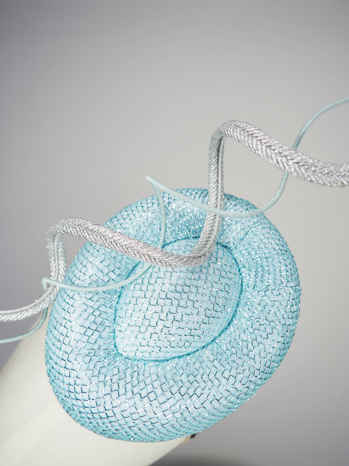 Blue Lagoon - A sophisticated pale aqua pillbox layered with shimmering lurex mesh and sculptural metallic swirls.