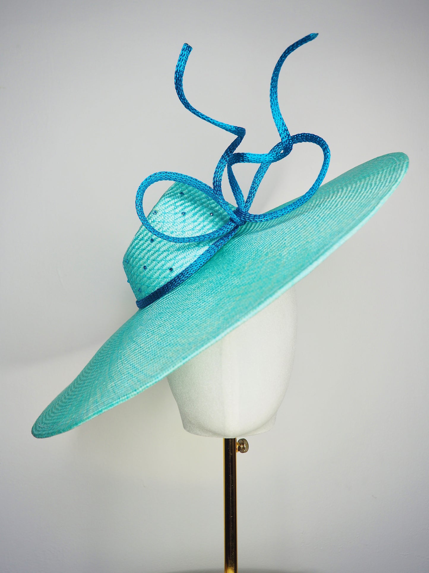 Sea Glass - A dramatic pale aqua asymmetrical brim featuring a sculptural turquoise bow, crystal detailing and delicate veiling.