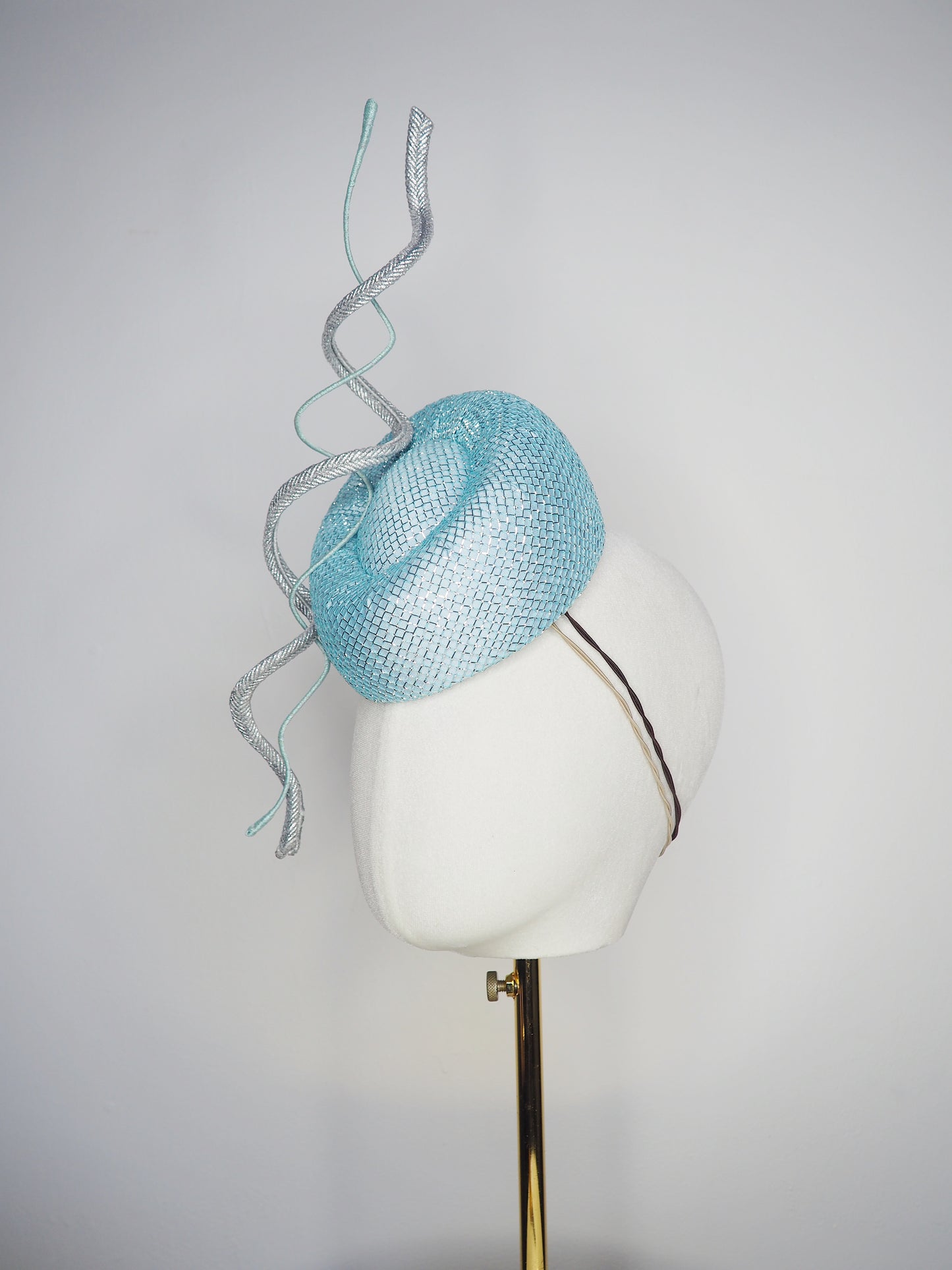 Blue Lagoon - A sophisticated pale aqua pillbox layered with shimmering lurex mesh and sculptural metallic swirls.