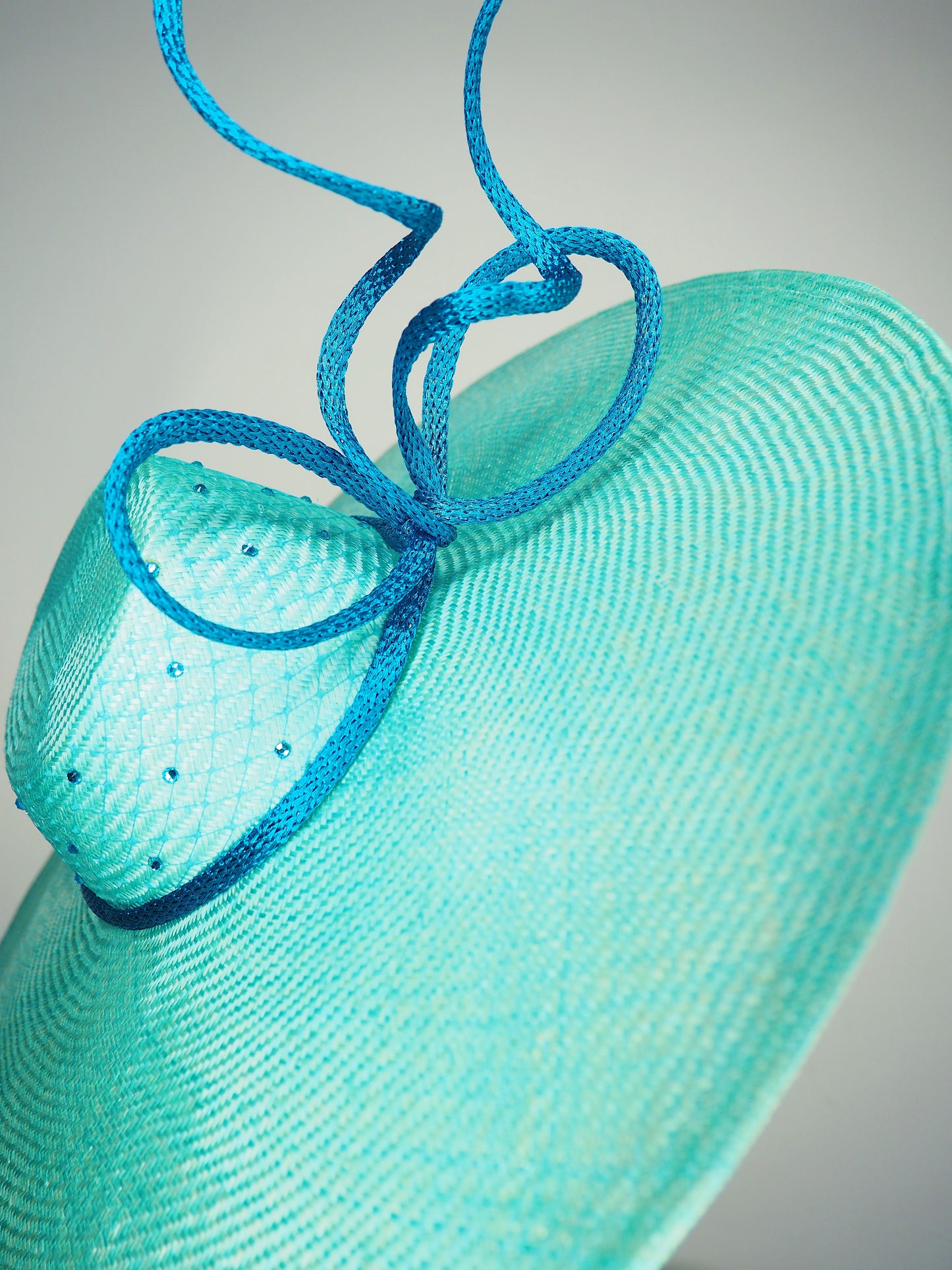 Sea Glass - A dramatic pale aqua asymmetrical brim featuring a sculptural turquoise bow, crystal detailing and delicate veiling.