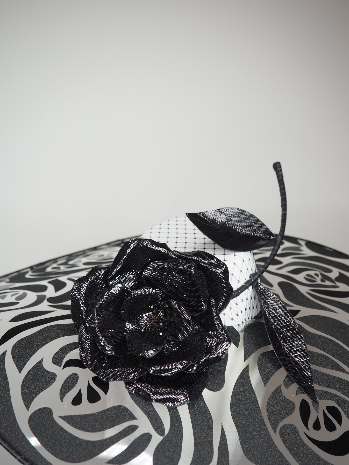 De Ville Rose - Sweeping crystoform wired brim with black rose petal pattern and single shiny dramatic rose with white leather veiled crown